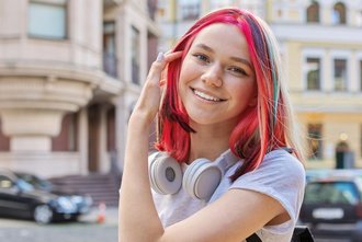 eine Jugendliche mit gefärbten Haaren und Kopfhörern lächelt